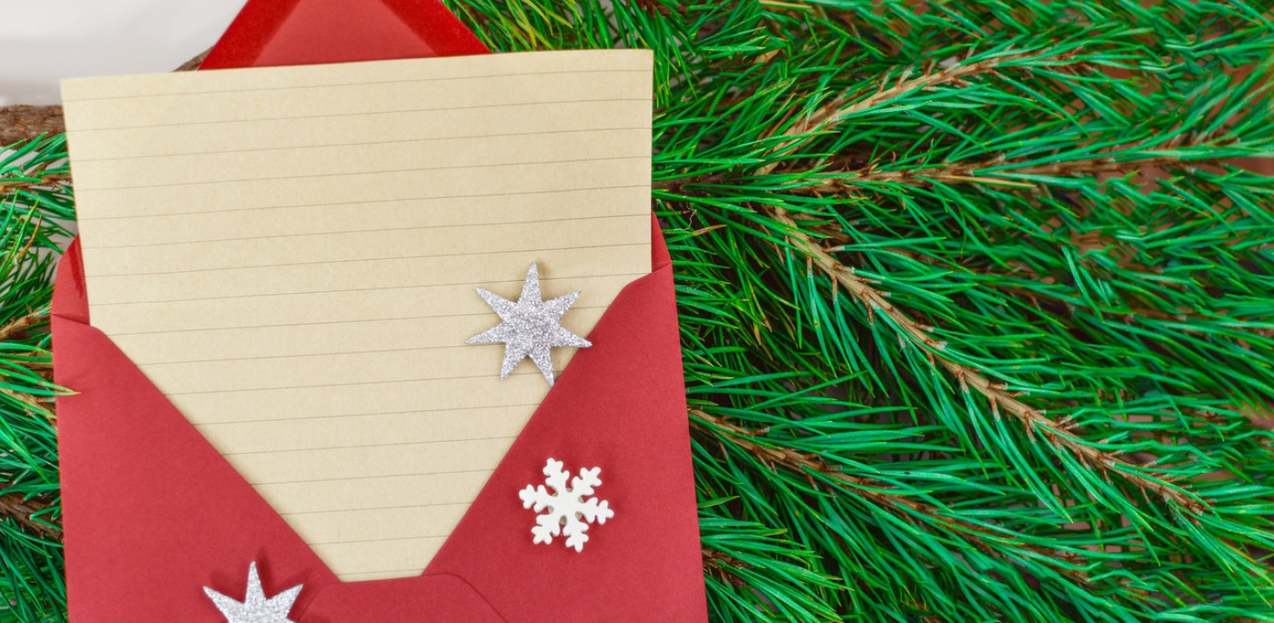 Note paper in a red envelope with snowflakes, laying on a bed of spruce