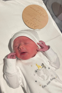 Baby Billy Isaac dressed in white baby-grow and hat laying in a cot