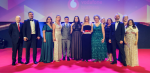 Emergency care staff standing on a stage. One woman in the centre of the group is holding a winner's trophy.
