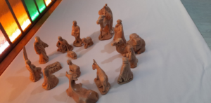 Small clay nativity scene on display on a white table by a stained glass window.