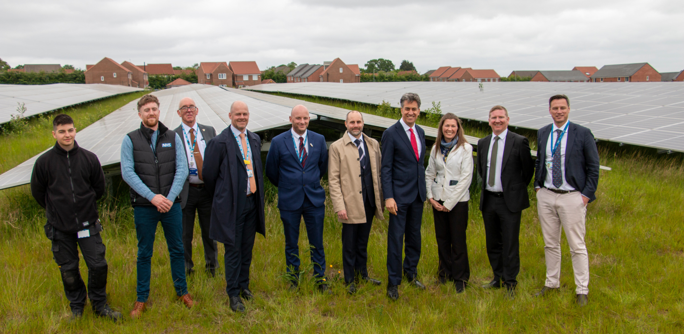 Group of people standing in a field in front of solar panels