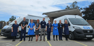 Members of the Hepatitis C screening team lined up standing between new mobile clinic vans