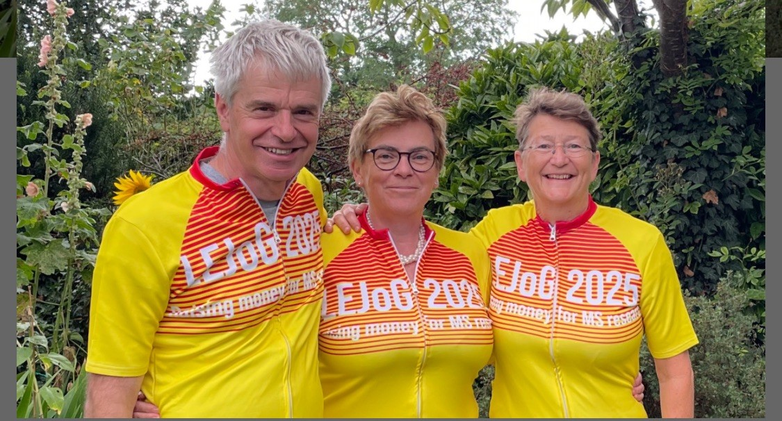 Adrian, Jacquie and Sarah wear their yellow cycling tops and stand in a line, arms around each other